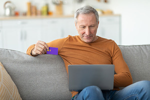 Casual mature man using pc and credit card at home, a Photo by Prostock-Studio
