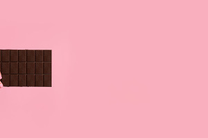 Woman’s hand holding a dark chocolate bar on soft pink backgro, a Food & Drink Photo by Ales Munt