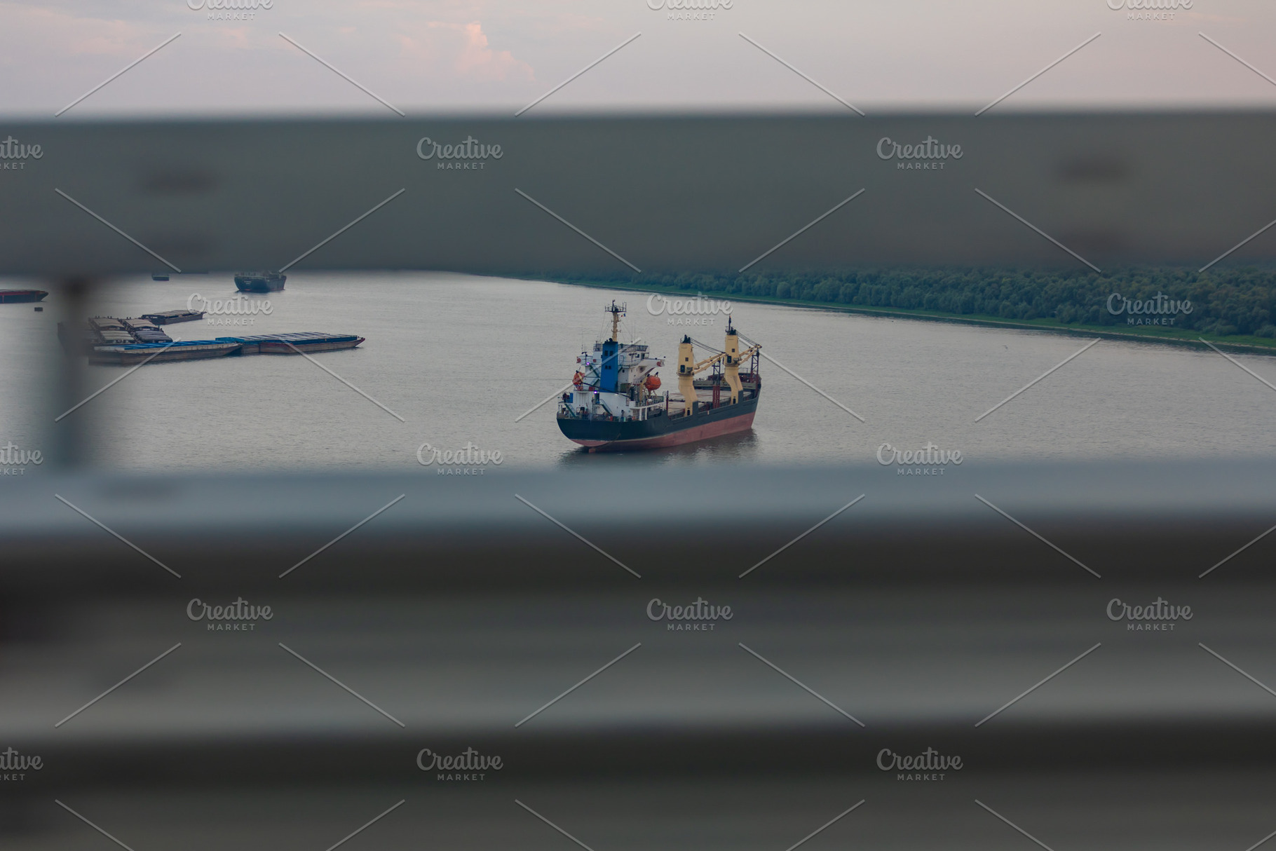 Large cargo ship anchored on a wide river, framed by blurred horizontal bars, w, a Transportation Photo by Ales Munt