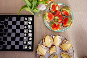 Assorted snacks and chess on a wooden table next to fresh tulips, a Photo by AS photostudio