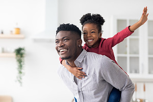 Happy black father piggybacking his pretty little daughter, a Photo by Prostock-Studio