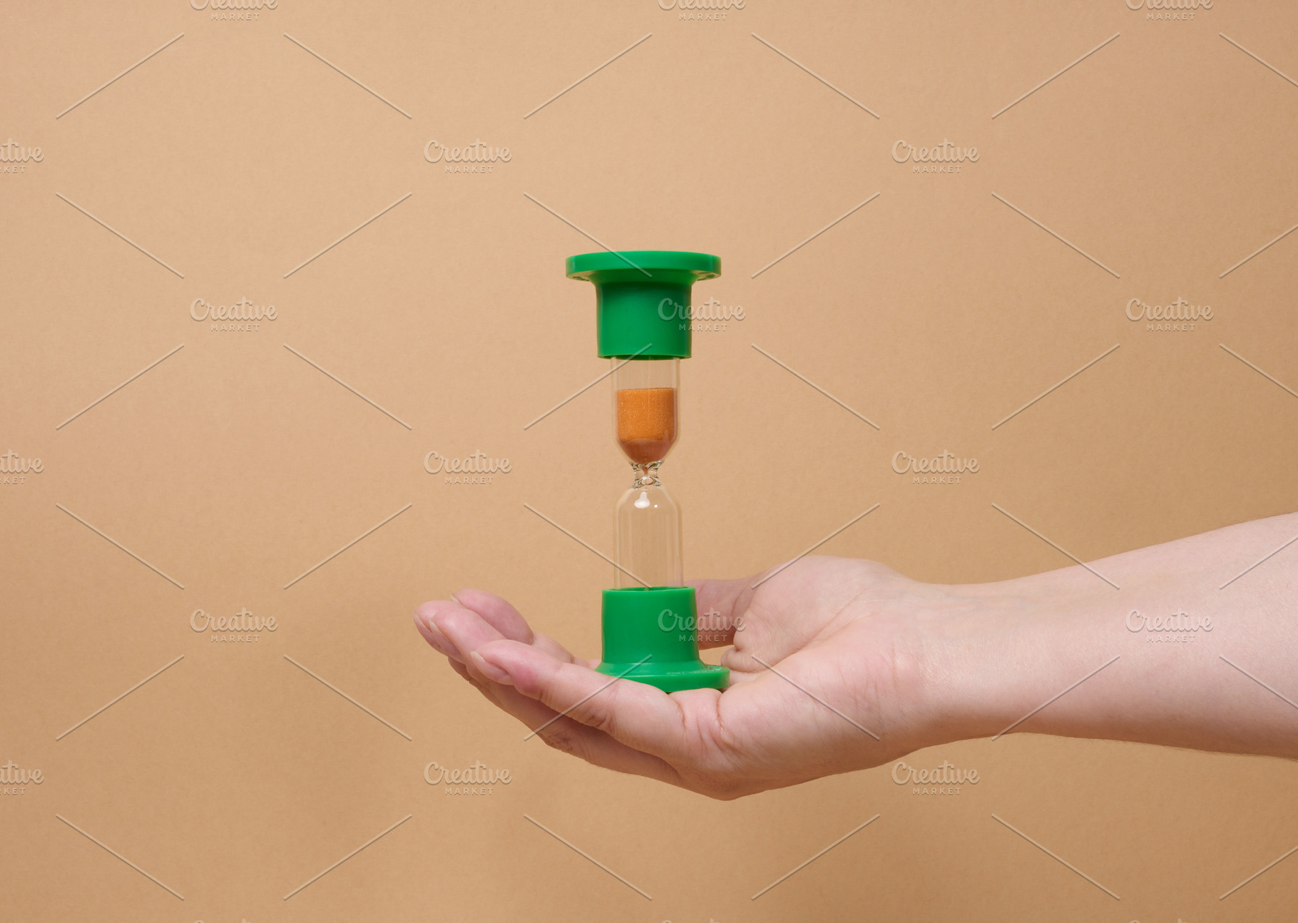 A person holding inverted green hourglass on their palm against, a Business Photo by ndanko
