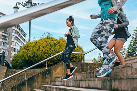 Young women friends training running down stairs in town