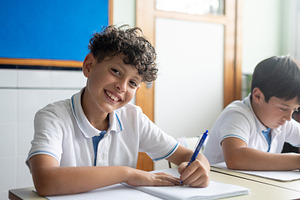 Elementary school boy smiling at the camera while writing in class, a Person Photo by etorres69