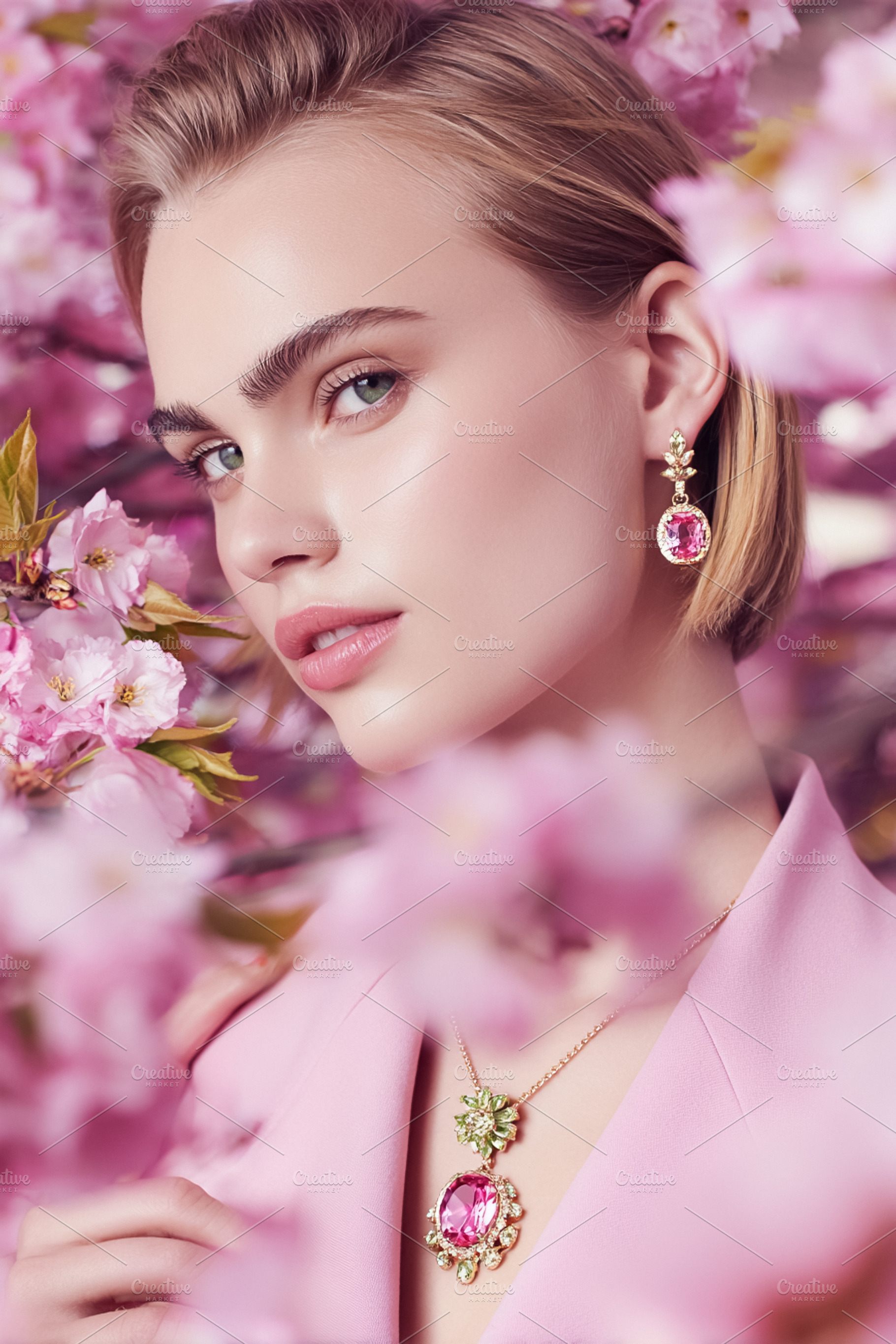 Young woman wearing pink gemstone jewelry among vibrant cherry b, a Photo by Studio ANNA