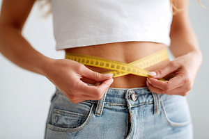 Woman measures her waist with a measuring tape while wearing casual clothing in, a Photo by AlyaAnd