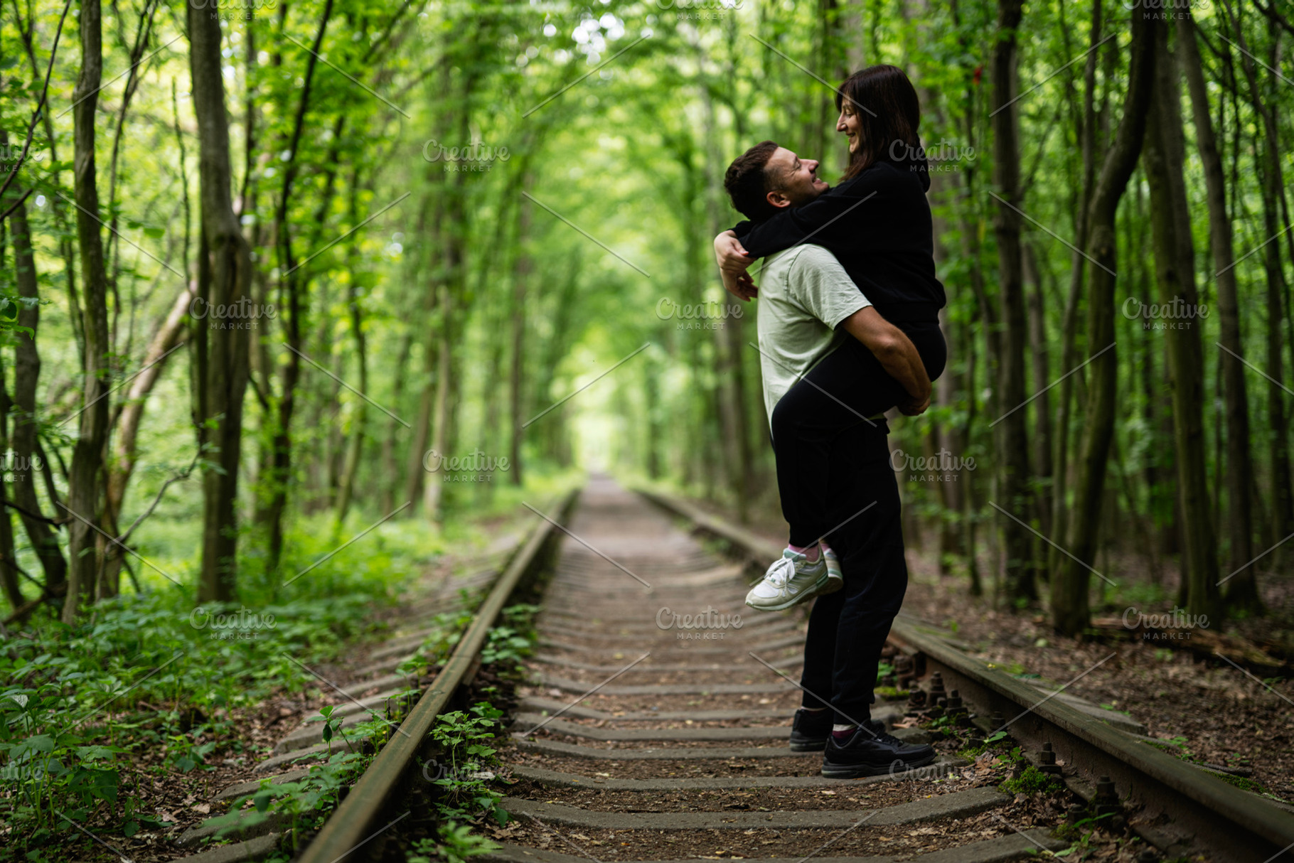 Romantic couple sharing a joyful moment on forest railway tracks, a Photo by AS photostudio