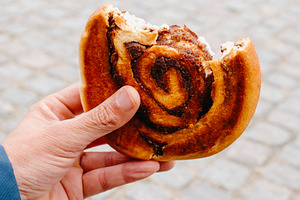 a man holding a bitten danish kanelsnegl, a Photo by Nito