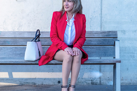 Blonde executive wearing red jacket sitting on a city bench while looking away, a Person Photo by 2Design
