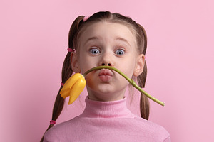 Happy young girl making a funny face with a yellow tulip against, a Person Photo by Ales Munt