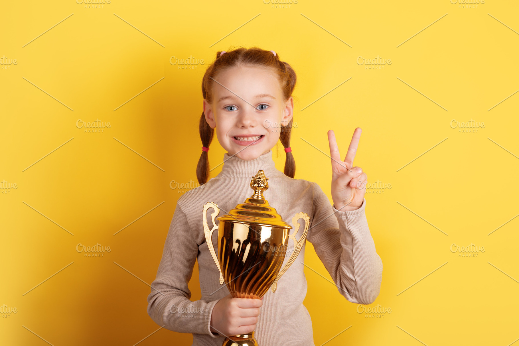 Smiling young girl with red hair holding a gold trophy and makin, a Person Photo by Ales Munt