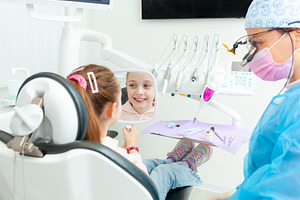 Little girl looking at her smile in the mirror at the pediatric dentist, a Photo by Antonio Gravante Market