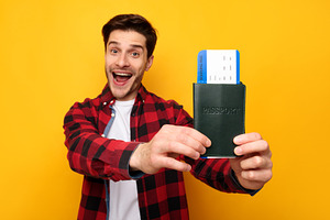 Excited young man holding showing tickets and passport