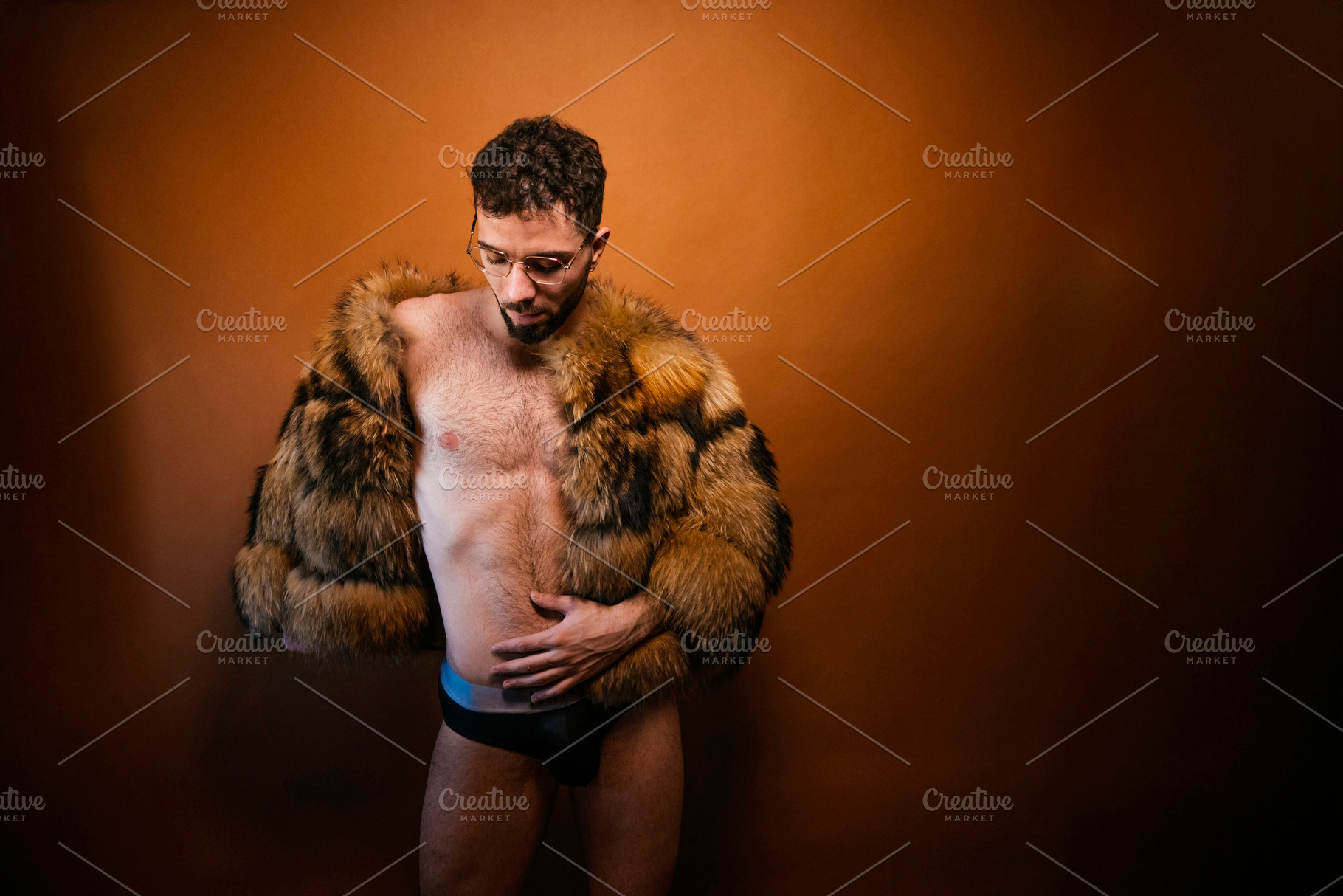 Confident man posing in faux fur jacket against orange background, a Photo by karrastock