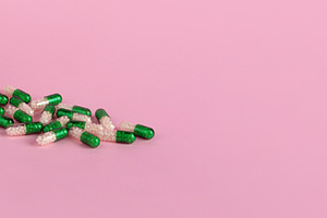 Open white bottle with green and white capsules spilling on past, a Health & Medical Photo by Ales Munt