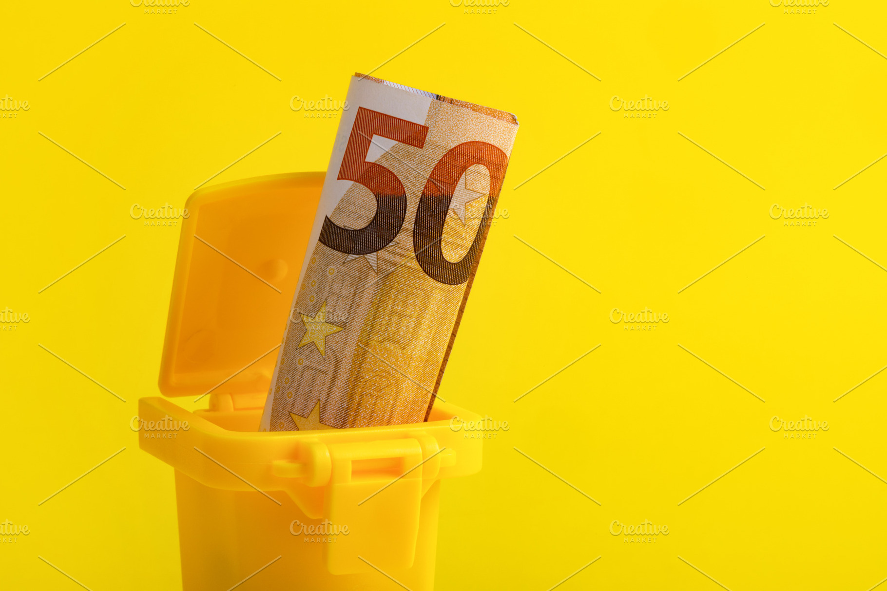 A fifty euro banknote placed in a small yellow trash bin against a vibrant yell, a Business Photo by Ales Munt