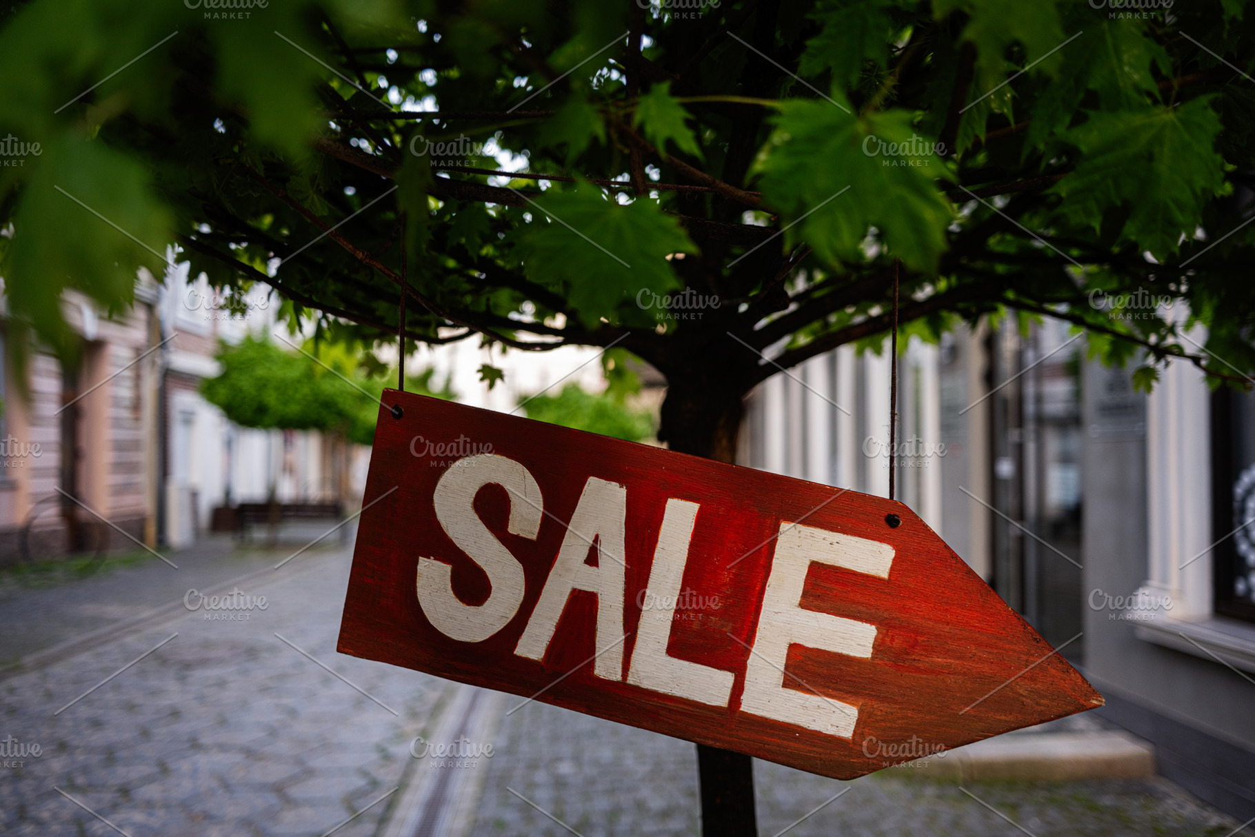 Red sale sign hanging on tree branch in urban street setting, a Photo by AS photostudio