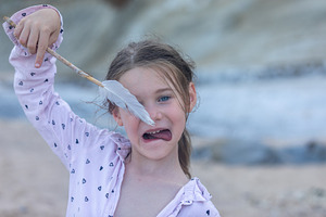 Smiling young girl holding a feather stick at the beach, making a funny face. N, a Person Photo by Ales Munt