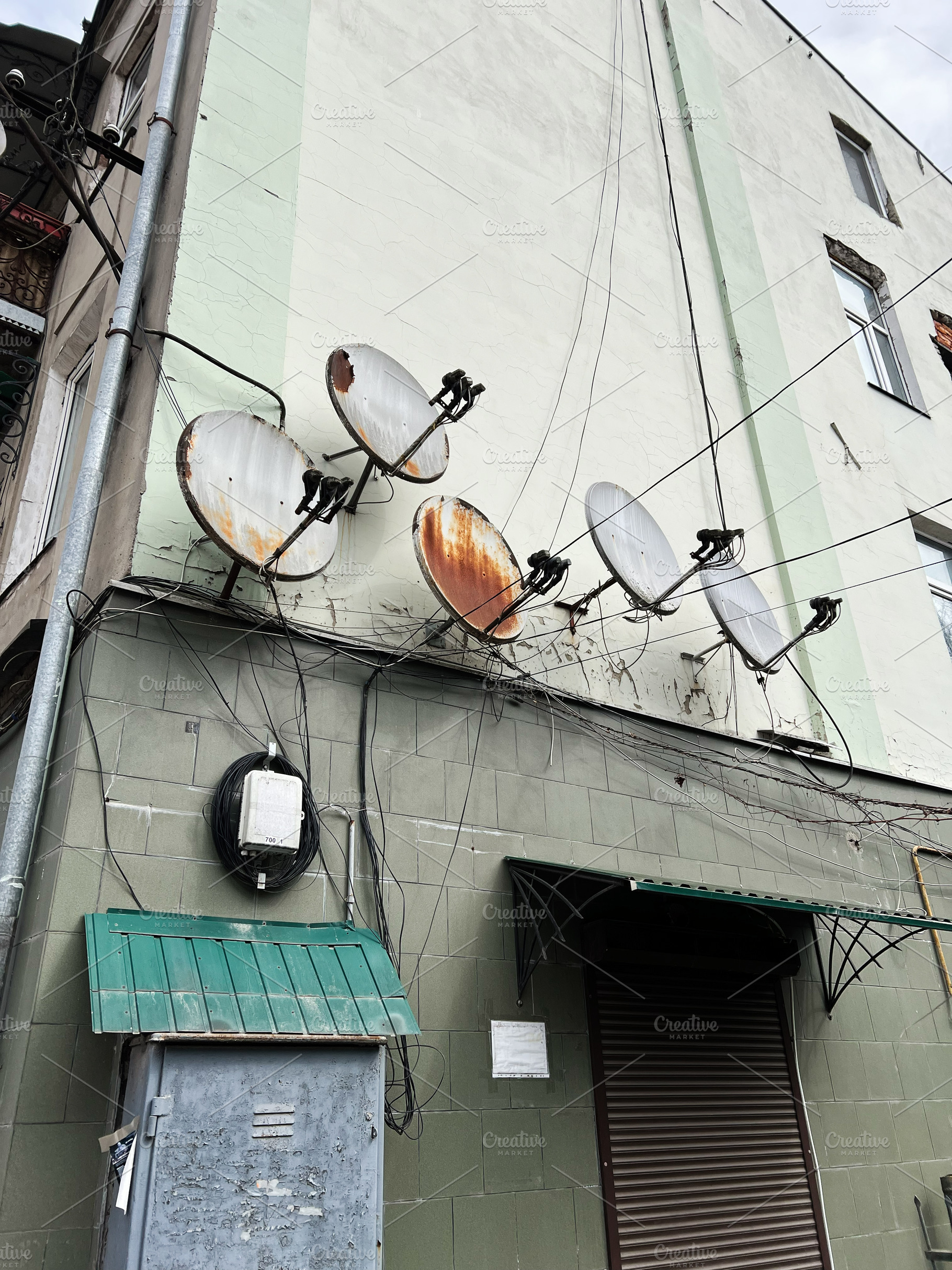Rusty satellite dishes on a building facade with attached electrical wires, a Photo by AS photostudio