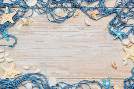Fishing net, starfishes and seashells framing rustic wooden back