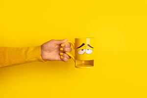 Hand in yellow sweater holding a yellow mug with a sleepy cartoo, a Food & Drink Photo by Ales Munt