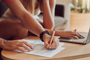 Couple calculating budget, finance and tax while planning investment, loan and bills on writing paper and laptop at home. Managing household spending, savings and insurance report for online banking, a Photo by Peopleimages.com
