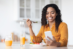 Happy black woman surfing on social media while having breakfast
