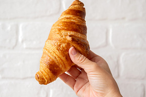 Hand Holding a Fresh Butter Croissant Against a White Brick Wall, a Food & Drink Photo by etorres69