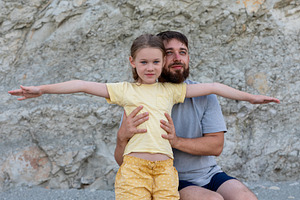 Father holding daughter as she stretches her arms wide, both smiling, against a, a Person Photo by Ales Munt