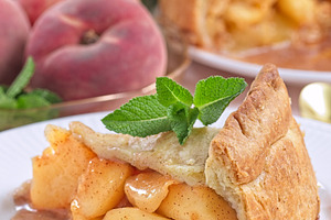 Delicious peach pie slice garnished with fresh mint, on white plate, vertical, a Food & Drink Photo by iuliia_n