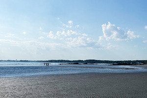 Sunny beach scene with calm water, rippled sand, and distant visitors, a Photo by AS photostudio