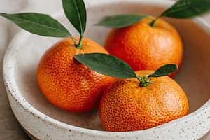 Handcrafted ceramic bowl holds fresh, bright oranges with leaves resting elegan, a Food & Drink Photo by AlyaAnd