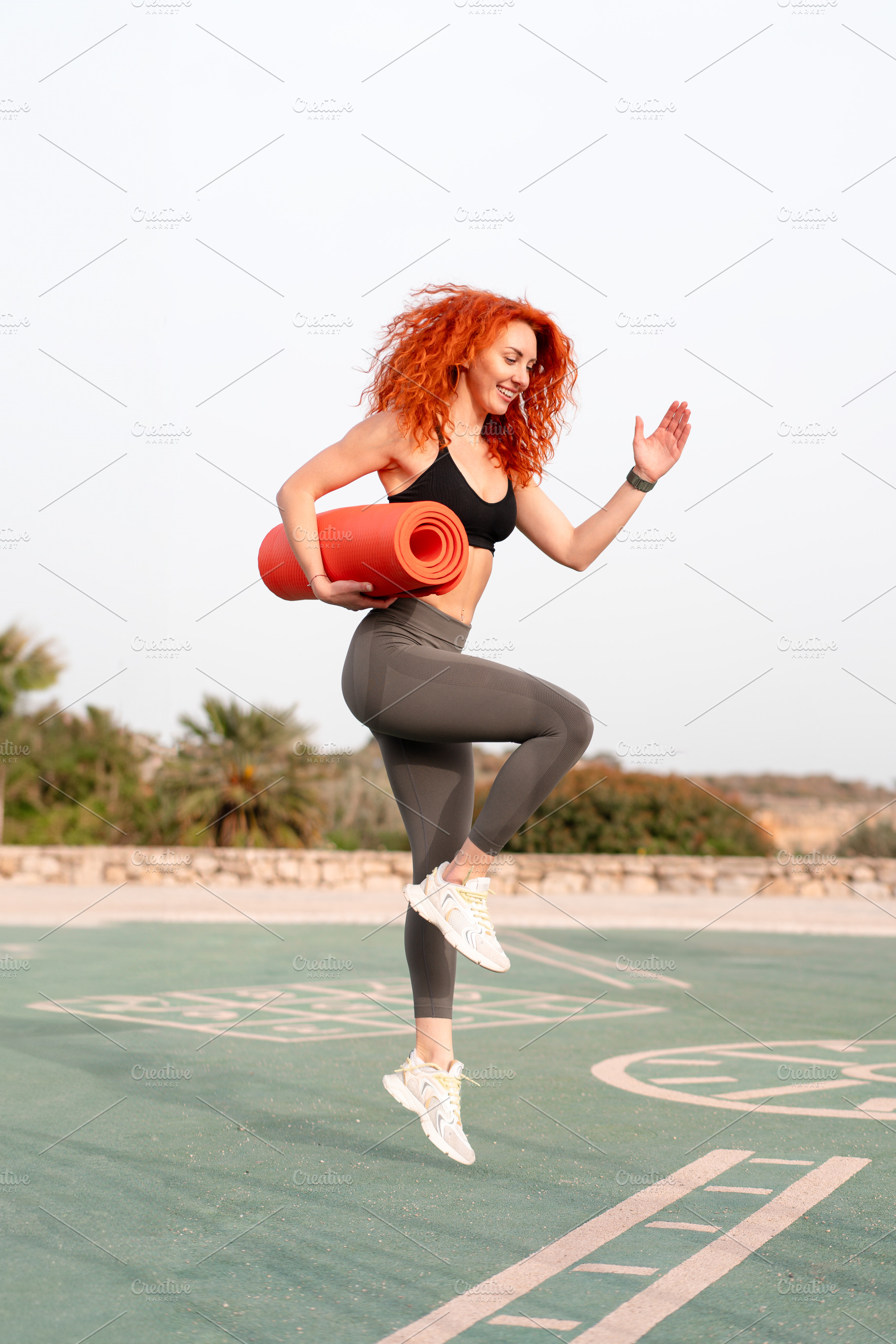 Happy jogger woman holding rolled up exercise mat at outdoor gym, a Person Photo by andreonegin market