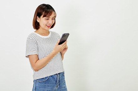 Smiling Asian woman using a smartphone, standing against texting on a mobile ph, a Person Photo by 1981 Rustic studio kan