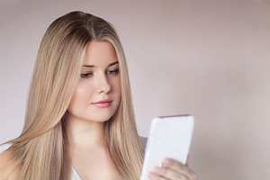 Young woman with long blonde hair looking down at a mobile phone, using a digit, a Person Photo by Studio ANNA