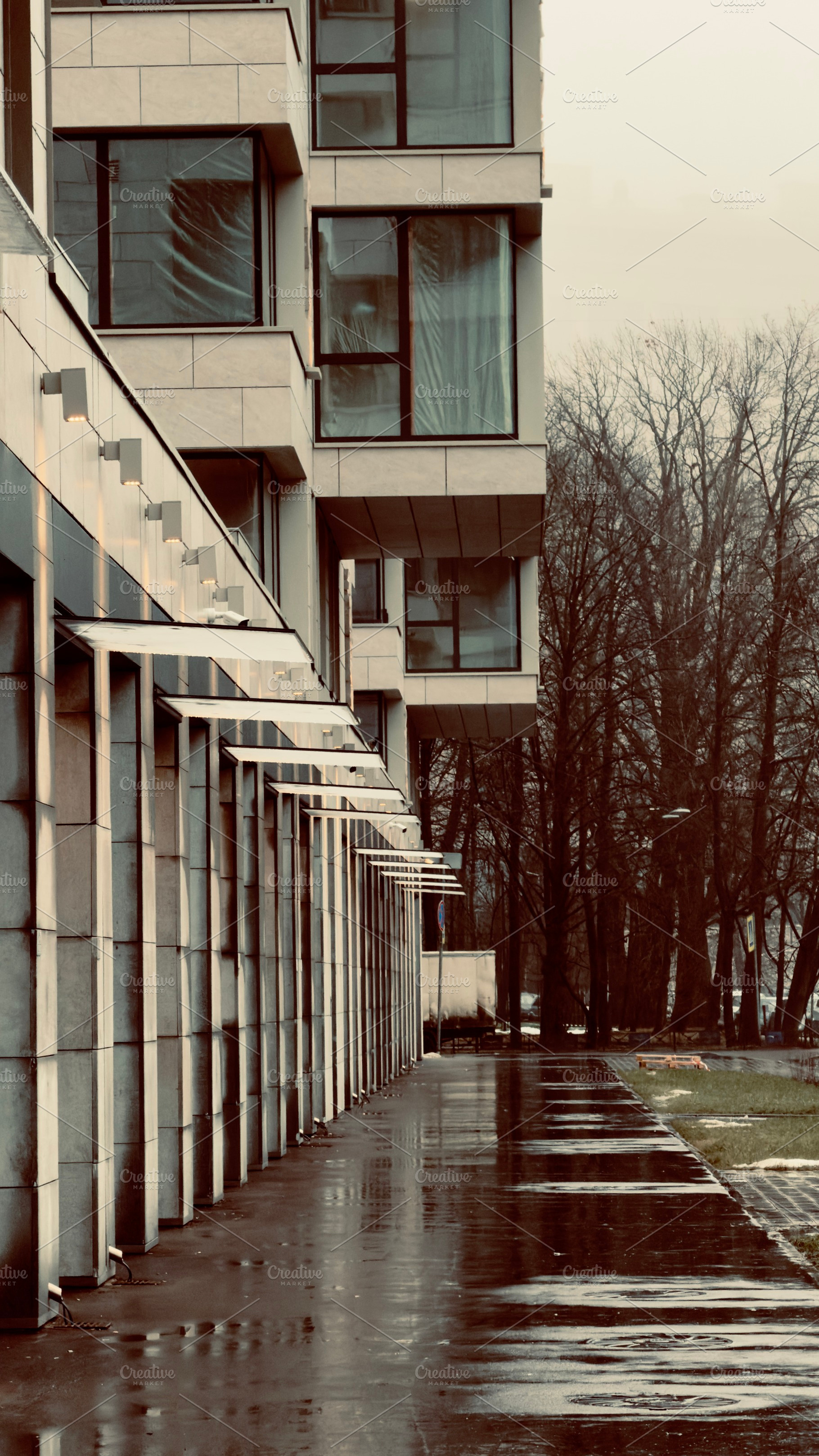 A modern building with large windows and a reflective wet sidewalk, surrounded, an Industrial Photo by Textures & Backgrounds