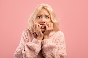 Afraid young lady biting nails with worry, having emotional stress, reacting to, a Photo by Prostock-Studio