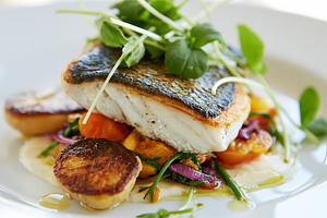 Seared sea bass fillet on a bed of roasted vegetables and scallops, garnished w, a Photo by Studio ANNA