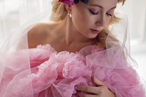 portrait of a fashionable blonde woman in a pink dress and rose flower in her h