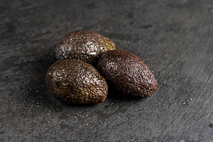 wet whole black avocado fruits of small size on a black slate, a Photo by rsoollAI