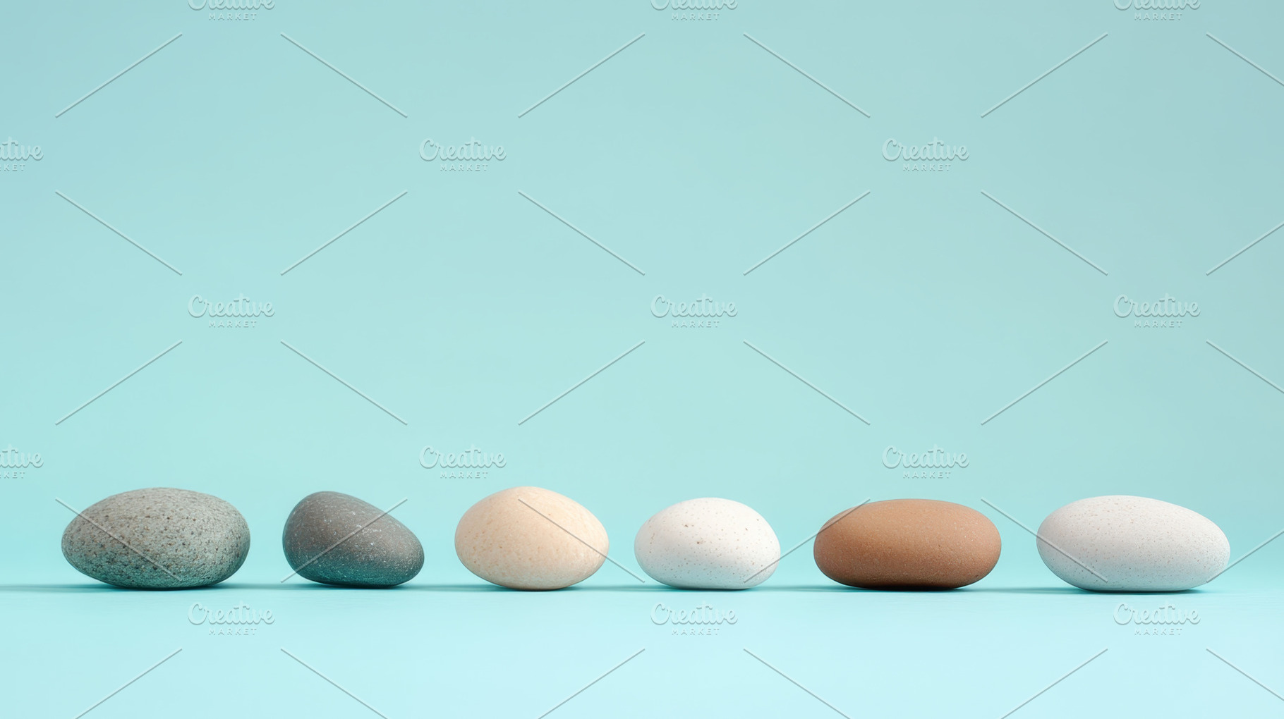 Assorted natural pebbles lined up on a light blue background, an Abstract Photo by Natalia Klenova's Shop