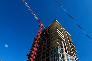 Red construction crane working at tall building under a clear blue sky, a Photo by AS photostudio