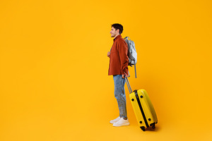 Traveler Guy With Travel Suitcase And Backpack On Yellow Background, a Photo by Prostock-Studio