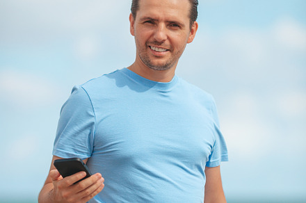 Young man holding mobile phone in his hand while walking on the beach, a Person Photo by travnikovstudio