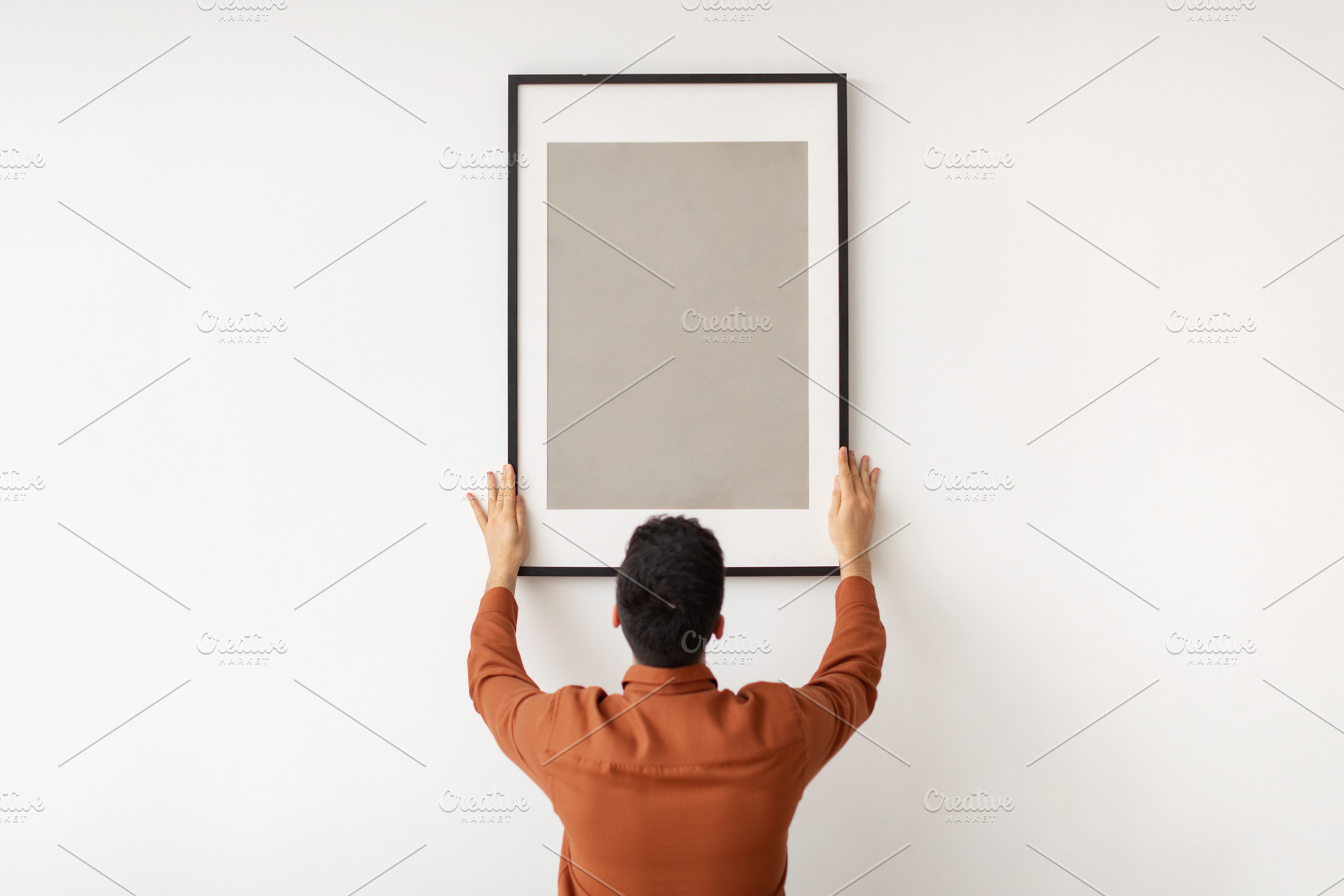 Young man hanging picture frame on the wall, a Photo by Prostock-Studio