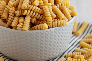 Uncooked Organic Dry Fusilli Pasta in a Bowl, side view., a Food & Drink Photo by LiudmylaChuhunova
