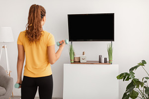 Lady Exercising With Dumbbells Watching TV At Home, Rear View, a Photo by Prostock-Studio