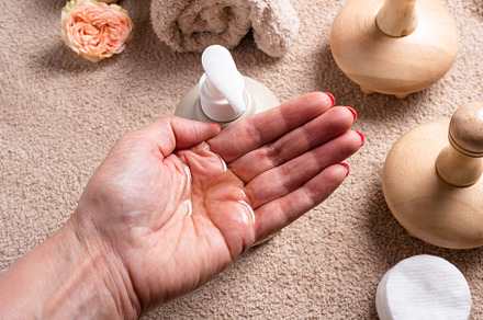 Woman hand holds oil, bottle with dispenser for massage oil on b