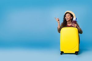 Carefree young black woman holding passport and tickets, sitting behind suitcas, a Photo by Prostock-Studio