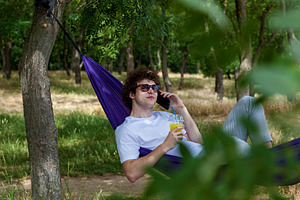 A young guy with curly hair is relaxing on a hammock on a hot summer day., a Person Photo by Photostock
